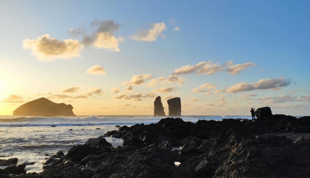 Stunning sunset at Mosteiros Beach, Açores, Portugal, with basalt rock formations and a lone photographer.