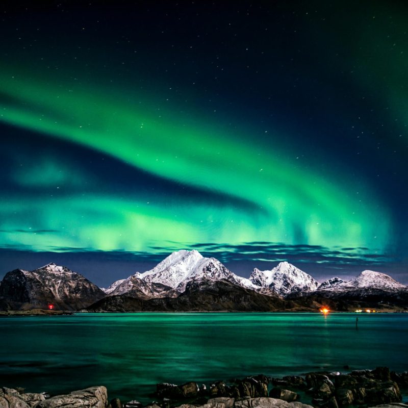 Breathtaking view of aurora borealis illuminating the snowy mountains of Lofoten Islands at night.